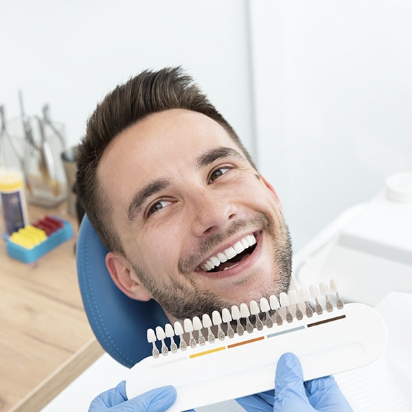 A man at the dentist smiling as the doctor checks the whiteness level of his teeth